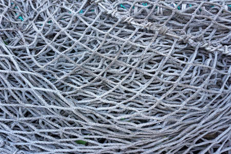 Old fishing nets. A closeup view of an old, faded white fishing net lying in a pile. A few bits of...