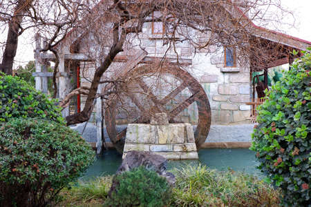 Water mill wheel on river on rainy day. Sustainable energy and water power traditional machinery