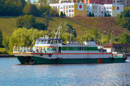 a river boat goes along a large river upstream, past the town on the bankの写真素材