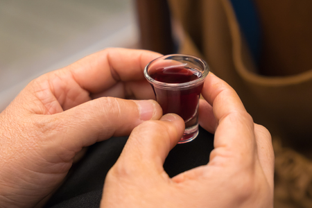 A lady's hands hold a red wine cup in Holy Communion.