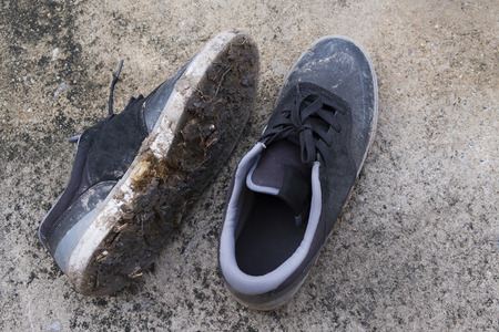 Muddy black sneakers on concrete floor.の写真素材