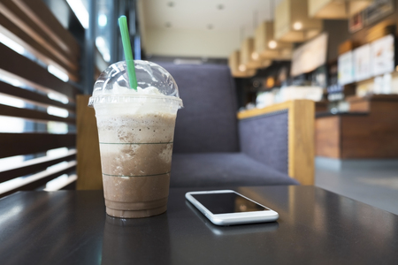 Cold mocha freppe coffee and white cellphone on coffee table in the coffee shop.の写真素材