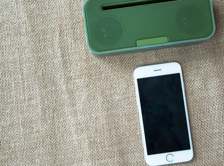 Green portable speaker and white smartphone on sackcloth background.の写真素材