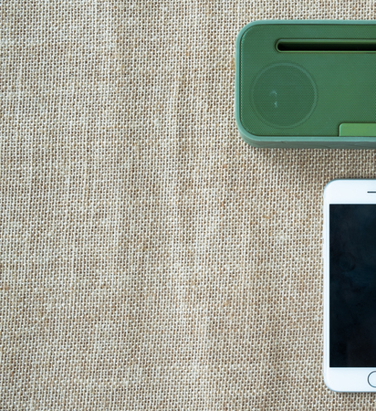 Green portable speaker and white smartphone on sackcloth background.