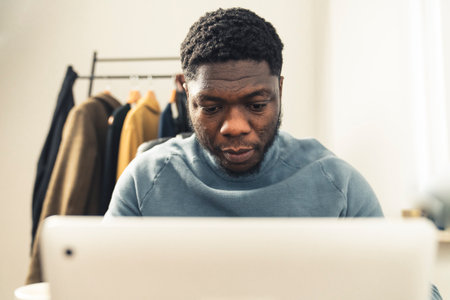 focussed intent black afroamerican working writing in front of white computer laptop tablet wearing light blue turtle neck long sleave - portrait shot. High quality photoの写真素材