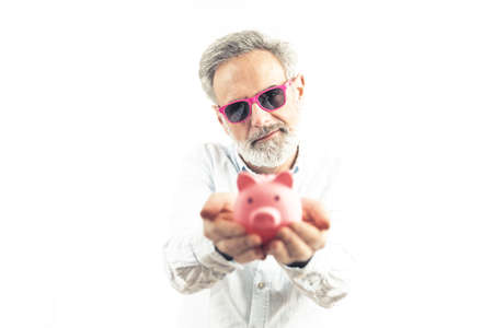 senior man in pink sunglasses holding the piggy bank - savings and happy retirement concept. High quality photoの写真素材