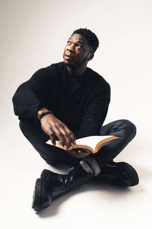 melancholic pensive black man sitting with a book - fullshot . High quality photo