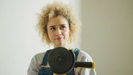 Pensive student girl holding a disc angle grinder - wondering crafty DIY projects. High quality...