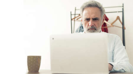 Gray haired bearded male enterprenuer in his 40s working on the computer - white background. High...