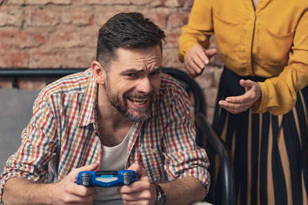 addicted caucasian man with a beard refuses to let go of the console pad and shouts at his elderly mother. High quality photoの写真素材