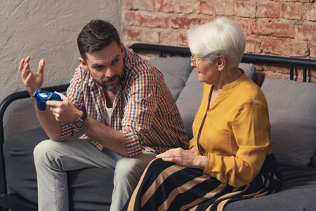 caucasian man in his 40s holding game pad gets angry with an elderly woman who interrupts his game. High quality photoの写真素材