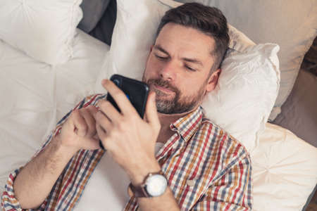 upset caucasian middle-aged man addicted to his phone and social media discovers unpleasant news. High quality photoの写真素材