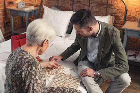 elderly grey-haired mother playing vocabulary games with her middle-aged caucasian son on bed. High quality photoの写真素材