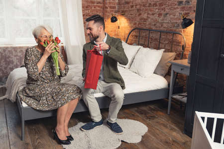 wide shot of a caucasian middle-aged man giving his mother beautiful red tulips and a present for Mothers Day . High quality photoの写真素材