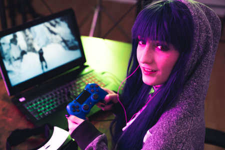 Young brunette in a hoodie uses gamepad and encourages to play with her medium close-up shot. High quality photoの写真素材