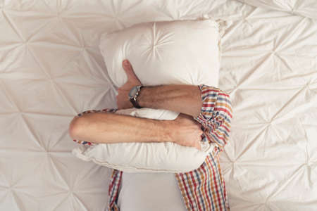 Portrait Of Caucasian Man Hugging A Pillow And Hiding His Face At Home. High quality photoの写真素材