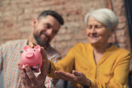 successful caucasian businessman learning his grandmother to save money using piggy bank. High quality photoの写真素材