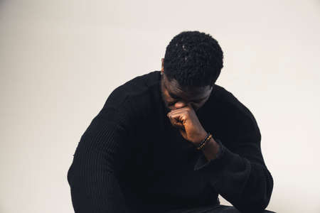 beaten man of color with fist in his face looking down white background - waist up shot. High-quality photoの写真素材