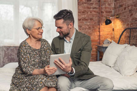 Content caucasian man showing new helpful application on tablet computer to his elderly mother. High quality photoの写真素材