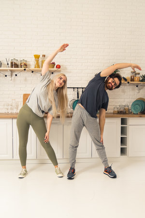 caucasian millennial couple stretching indoors in their bright apartment to built body strength vertical shot. High quality photoの写真素材