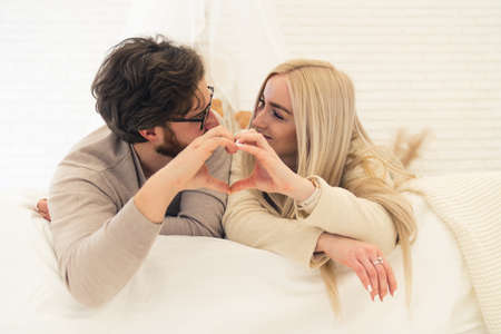 cute young European married couple laying on bed and forming heart shape with their hands, concept of love. High quality photoの写真素材