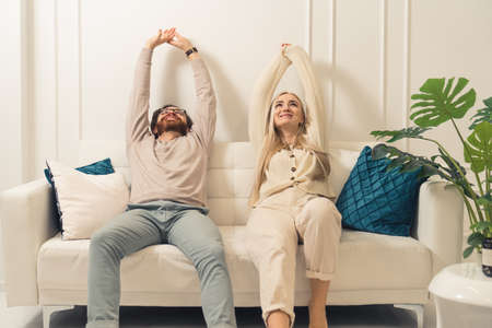Calm lazy caucasian couple relaxing together on comfortable sofa and stretching their arms in the air. High quality photoの写真素材