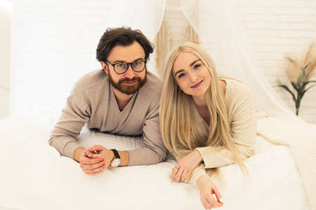 young entrepreneur and his beautiful businesswoman girlfriend laying down on their bed, smiling, and looking at camera. High quality photoの写真素材