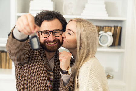 young caucasian entrepreneur got his first car, holds car keys in the air, and is kissed by his beautiful fiancee. High quality photoの写真素材