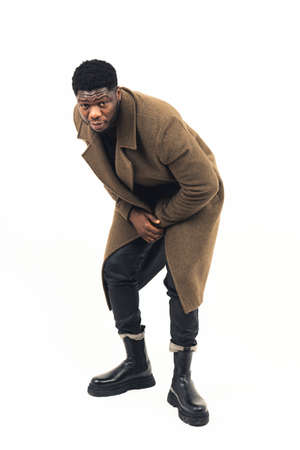 Afroamerican man bending and posing brown coat white background - full shot. High-quality photoの写真素材