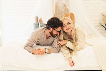 cheerful brunet with his lovely long-haired girlfriend laying on bed, joking, and smiling. High quality photoの写真素材