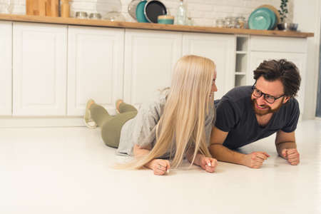 young adults couple doing plank pose on white floor in the kitchen to built body strength. High quality photoの写真素材