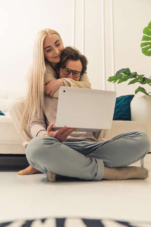 vertical shot of a cute caucasian couple sitting on the floor and happily looking on the laptops screen and browsing the internet. High quality photoの写真素材