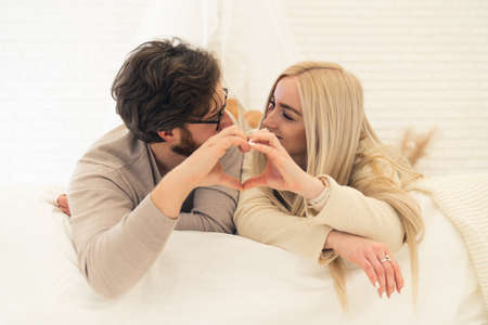 Cute Caucasian Couple Looking At Each Other Forming Heart Shape With Their Palms While Laying On Their Bed. High quality photoの写真素材