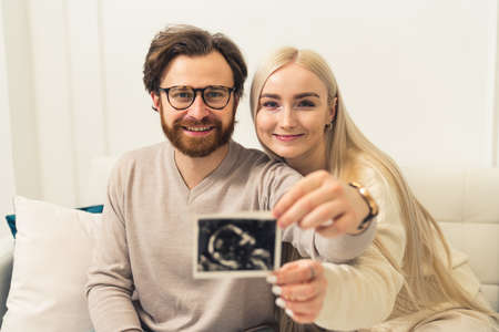 Happy caucasian married couple showing pregnancy ultrasound picture of their unborn baby. . High quality photoの写真素材