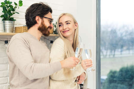 two caucasian people celebrating their relationship and drinking champagne from beautiful glasses while standing next to the window. High quality photoの写真素材