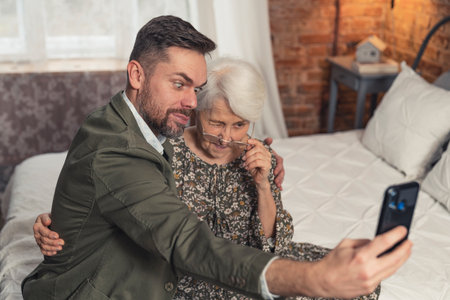 elderly grandmother and her oldest grandson making silly faces and taking a selfie with black smartphone. High quality photoの写真素材