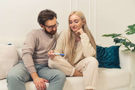 caucasian businessman finds out that his blonde long-haired fiancee is pregnant by looking at a pregnancy test results. High quality photoの写真素材
