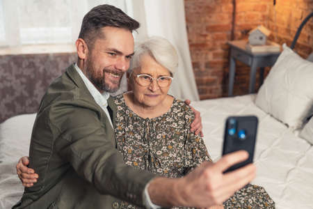 relatives middle-aged bearded elegant son with his elderly pensioner mother taking a selfie. High quality photoの写真素材