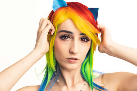 European flirty Cosplayer woman in rainbow wig posing with her hands near to her face isolated . High quality photoの写真素材