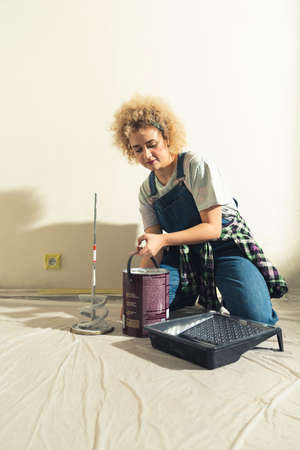 curly hair caucasian girl in dungarees pouring the paint onto the paint tray. High quality photoの写真素材