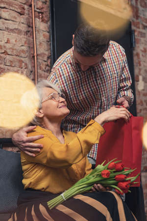 elderly European woman pleasantly surprised by her middle-aged son giving her flowers and a present . High quality photoの写真素材