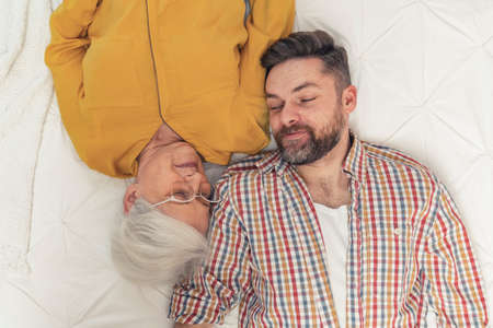 caucasian short-haired grandma laying down with her adult grandson and looking at each other top shot portrait. High quality photoの写真素材
