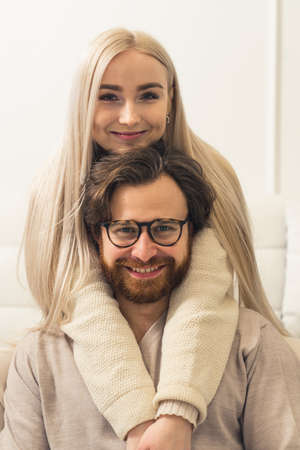 Happy European Couple Concept. Millennial blonde long-haired woman cuddling the head of her brunet bearded partner who is sitting in front of her. Vertical Shot. High quality photoの写真素材