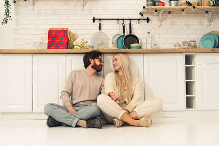 beautiful caucasian long-haired woman sitting on the floor in the kitchen together with her beloved husband wide indoors shot. High quality photoの写真素材
