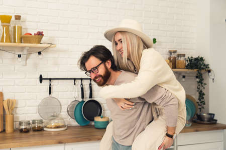 young caucasian bearded man giving young blonde long-haired woman in a hat piggyback. High quality photoの写真素材