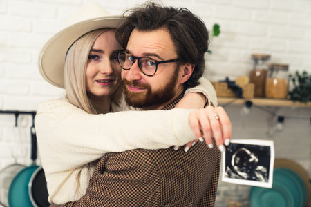 future caucasian parents hugging and showing ultrasound picture of their baby to the camera. High quality photoの写真素材