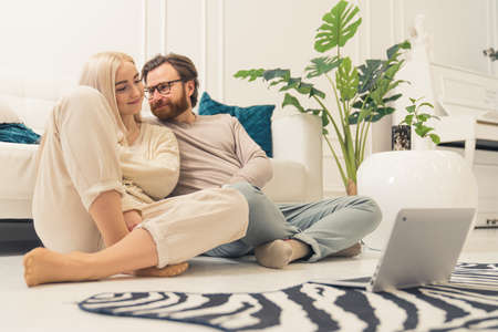 Loving caucasian young couple sitting on the floor at home with their brand new laptop. High quality photoの写真素材