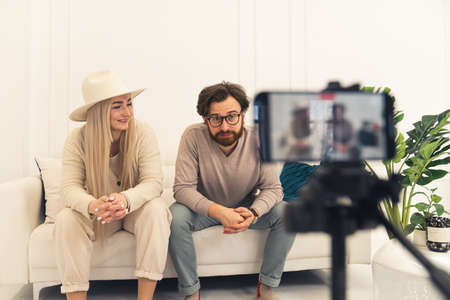 cheerful European influencers creating a new video while sitting on a white couch in their modern flat. High quality photoの写真素材