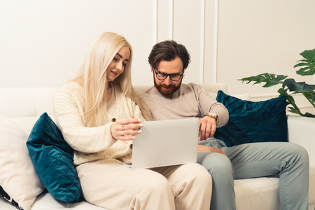 Happy woman browses laptop in new modern flat, while her intrigued boyfriend points at the screen. High quality photoの写真素材