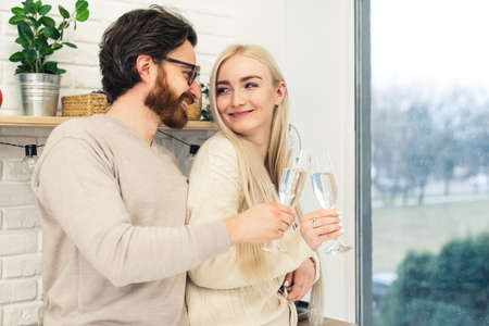 young couple smiling at each other celebrating their anniversary in the kitchen by drinking champagne . High quality photoの写真素材